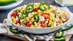 a white bowl filled with corn and vegetables on top of a wooden cutting board next to green peppers