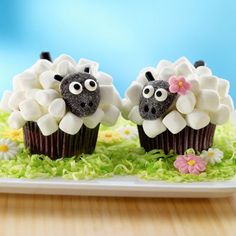 two cupcakes decorated like sheep sitting on top of green grass