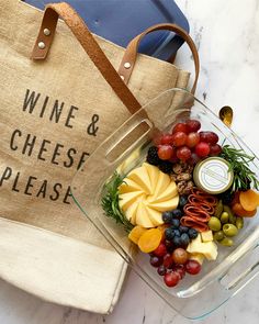 a glass bowl filled with grapes, cheese and crackers next to a wine bag