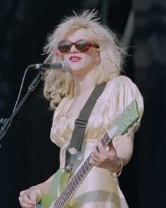 a woman wearing sunglasses and holding a guitar in front of a microphone