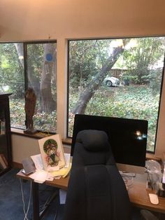 an office with two large windows and a desk in front of the window is a black chair