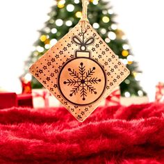 a christmas ornament hanging on a red blanket with a tree in the background