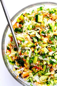 a glass bowl filled with chopped vegetables on top of a white tablecloth next to a metal spoon