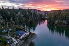 an aerial view of a lake surrounded by trees and houses at sunset with the sun setting in the distance