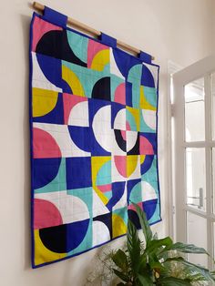 a colorful quilt hanging on the wall next to a potted plant