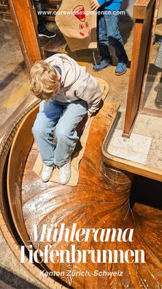 a young boy sitting on top of a wooden table in front of a mirror next to another person