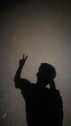 a person standing in the dark with their shadow on the ground and hand raised up