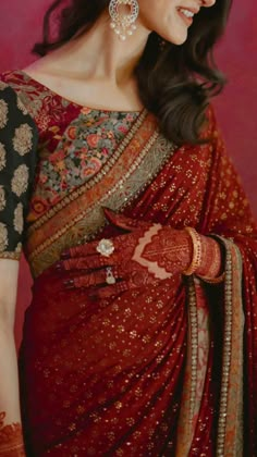 a woman in a red and black sari with gold jewelry on her neck, smiling at the camera