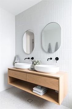 two round mirrors on the wall in a white bathroom with wooden vanity and double sinks