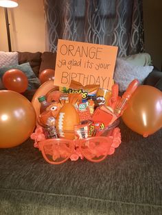 an orange birthday gift basket with balloons and confetti on the table in front of it