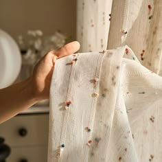 a person holding up a curtain in front of a window with beading on it