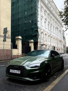 a green car is parked on the side of the road in front of a building