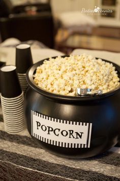 a black bowl filled with popcorn sitting on top of a table next to paper cups