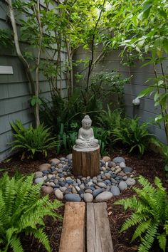 a small buddha statue sitting on top of a wooden stump in a garden filled with plants