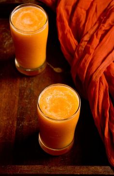 two glasses filled with orange juice next to an orange blanket