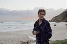 a man standing on top of a beach next to the ocean holding a drink in his hand