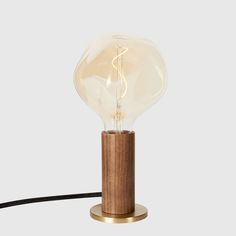 a wooden table lamp with a light bulb on it's end and a cord running through the middle