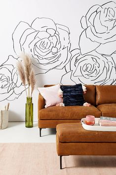 a couch and ottoman in front of a wall with flowers painted on the wall behind it