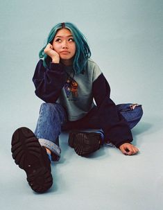 a woman with blue hair sitting on the ground wearing black sneakers and a green sweater