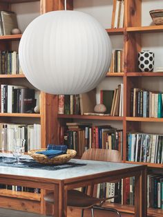 a dining room table with bookshelves and a large white ball hanging from the ceiling