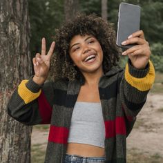 a woman holding up her cell phone in front of her face and making the peace sign