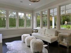 a living room filled with white furniture and lots of window paned in the background