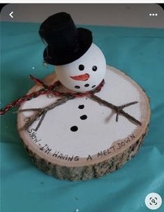 a snowman is sitting on top of a piece of wood that has writing on it