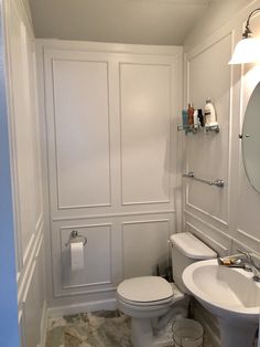 a white toilet sitting next to a sink in a bathroom under a mirror and light