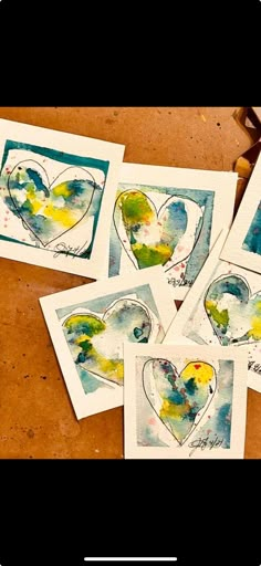 four cards with watercolors on them sitting on a table next to some scissors