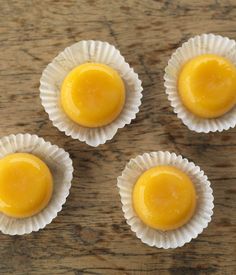 four cupcakes sitting on top of white paper cups with yellow icing in them