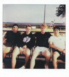 four young men sitting next to each other on a bench