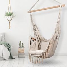 a hammock chair hanging from a wall next to a white bed and nightstand