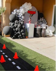 an outdoor party with black and white decorations on the grass, orange cones and balloons