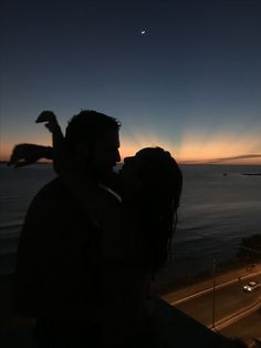 a man and woman standing next to each other near the ocean at sunset with an airplane in the sky