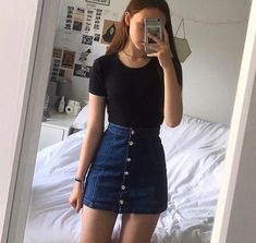 a woman taking a selfie in front of a mirror while wearing a black shirt and denim skirt