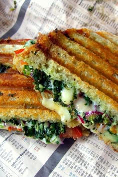 a sandwich cut in half sitting on top of a piece of paper covered in cheese and vegetables