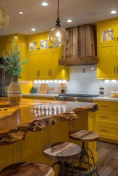 a kitchen with yellow cabinets and stools in front of an island counter top that has wood slices on it