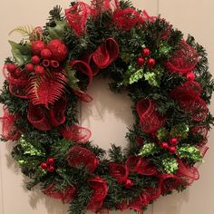 a christmas wreath hanging on the wall with red bows and greenery in front of it