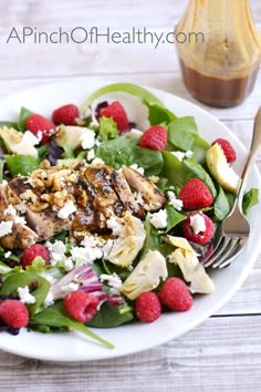 a salad with chicken, raspberries and feta cheese is on a white plate