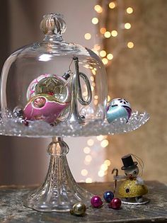 there is a glass cake stand with ornaments on it