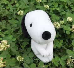 a white stuffed dog sitting in the middle of some clover covered grass and flowers with its eyes closed