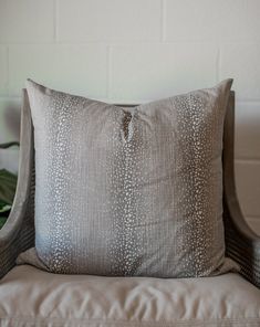 a gray pillow sitting on top of a chair next to a green potted plant