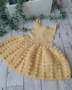 a crocheted yellow dress sitting on top of a wooden floor next to a potted plant