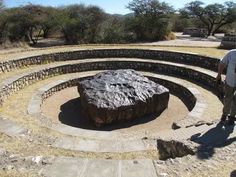 a man standing next to a large rock in the middle of a circle shaped area