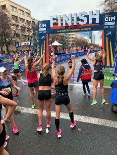 a group of women standing in front of a finish line with their arms up and hands in the air