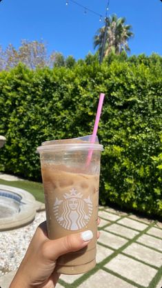 a person holding up a starbucks drink in front of some bushes and shrubbery on a sunny day