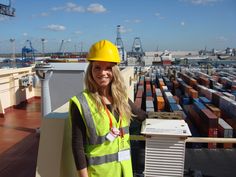 a woman wearing a hard hat and safety vest standing on top of a container ship