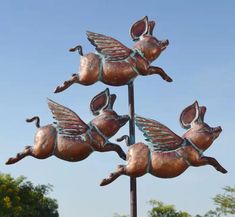 a metal weather vane with four flying pigs on it's back and wings in the air