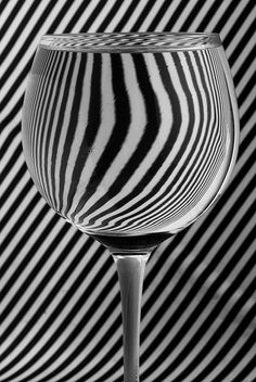 a wine glass sitting in front of a black and white striped wall with vertical stripes