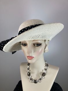 This spring/summer neutral women's asymmetrical brim hat is so pretty! The color is off white with an open weave for coolness. It is completely handmade, hand blocked and one of a kind. The hat is embellished simply, with a black and white polka dot band that is tied into a loose bow. Her name is Brianna. A pretty coordinating braid encircles the brim, which is three 1/2 to four inches wide, tapering to 2 1/2 inches wide at the back. A great ladies hat that stands apart from mass produced ones. Elegant Lightweight Brimmed Panama Hat, Elegant Lightweight Hats For Spring, Elegant Lightweight Panama Hat, Chic Lightweight Cream Hat, Elegant Lightweight Spring Hats, Elegant Lightweight Panama Hat With Flat Brim, Classic White Sun Hat For Summer, White Brimmed Cloche Hat For Garden Party, White Summer Hat For Kentucky Derby